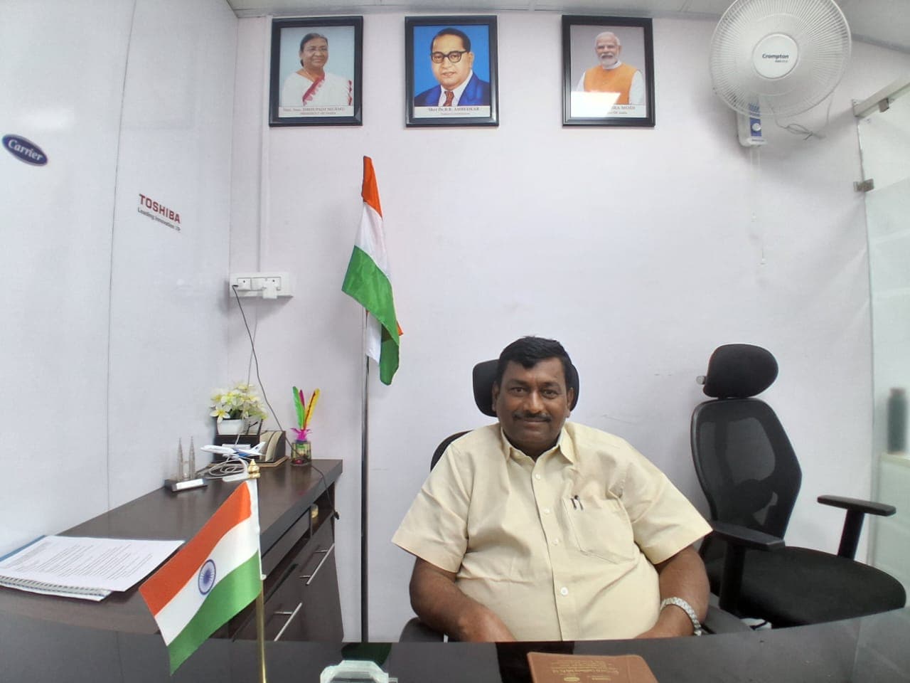 Wide-angle photograph of the interior of the Tribal Area Service Society (TASS) office in Kakinada, featuring the main desk, office seating, and official organizational signage on the wall.